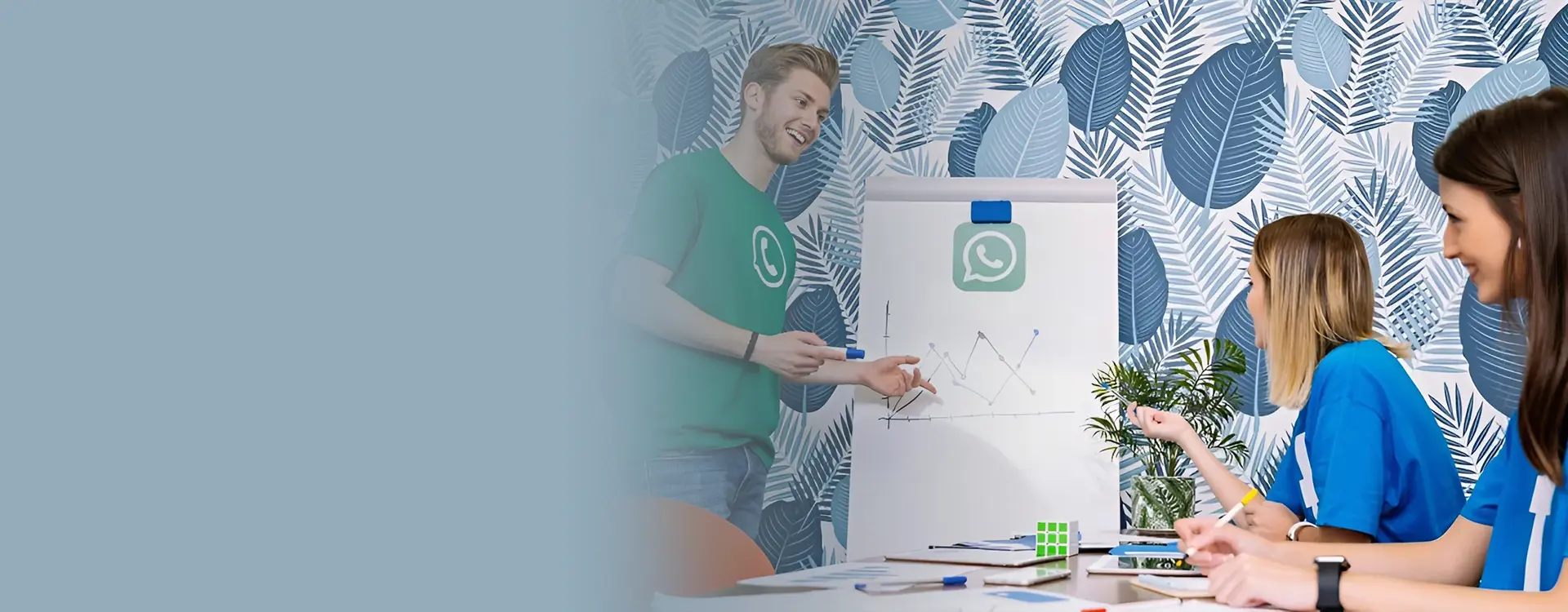 A team meeting in progress with a presenter explaining a graph on a flip chart to his engaged colleagues in a vibrant, leaf-patterned office.