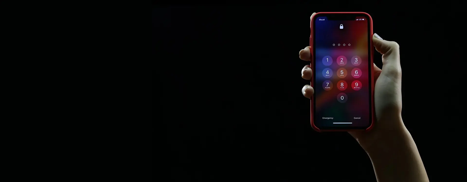 Hand holding a smartphone with the screen displaying a lock screen keypad against a dark background.