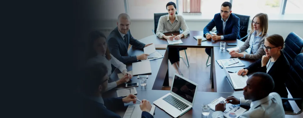 Professionals engaged in a boardroom meeting, discussing important matters around the conference table with laptops and documents at hand.