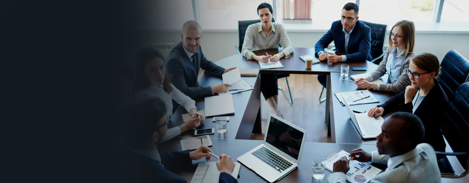 Professionals engaged in a boardroom meeting, discussing important matters around the conference table with laptops and documents at hand.