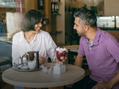 A cheerful couple enjoying a casual coffee date, sharing laughter over a sweet dessert in a cozy cafe.