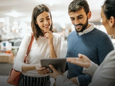 A couple attentively listening to a salesperson who is explaining a product using a digital tablet in a retail store.