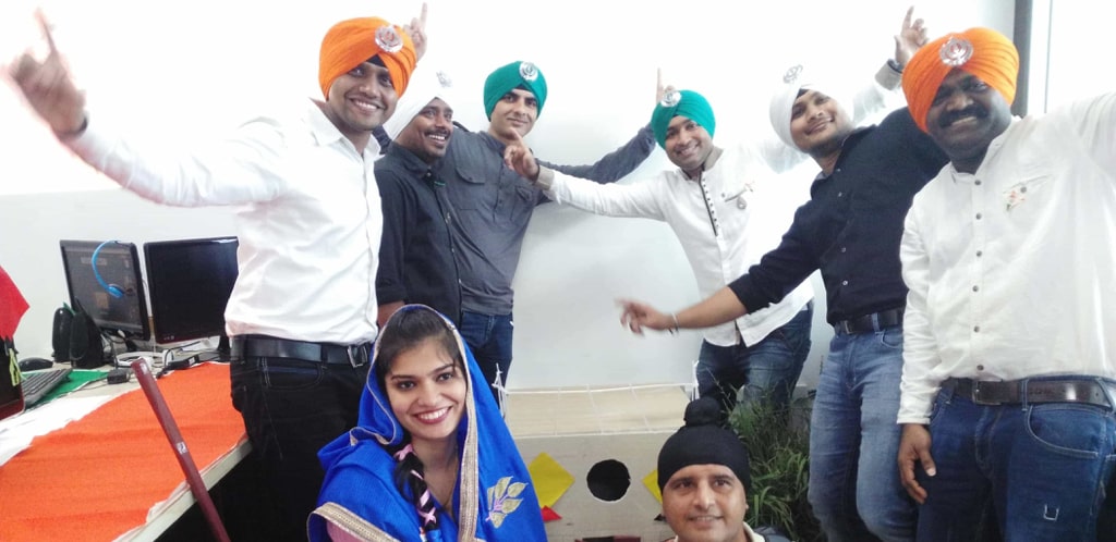 A joyous group of people celebrating, with some wearing traditional sikh turbans, possibly at a cultural or office event.
