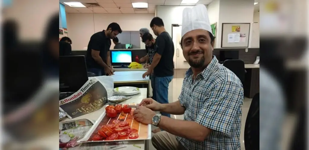 a man wearing a chef's hat while skillfully cutting tomatoes on an office desk with colleagues working in focalworks.