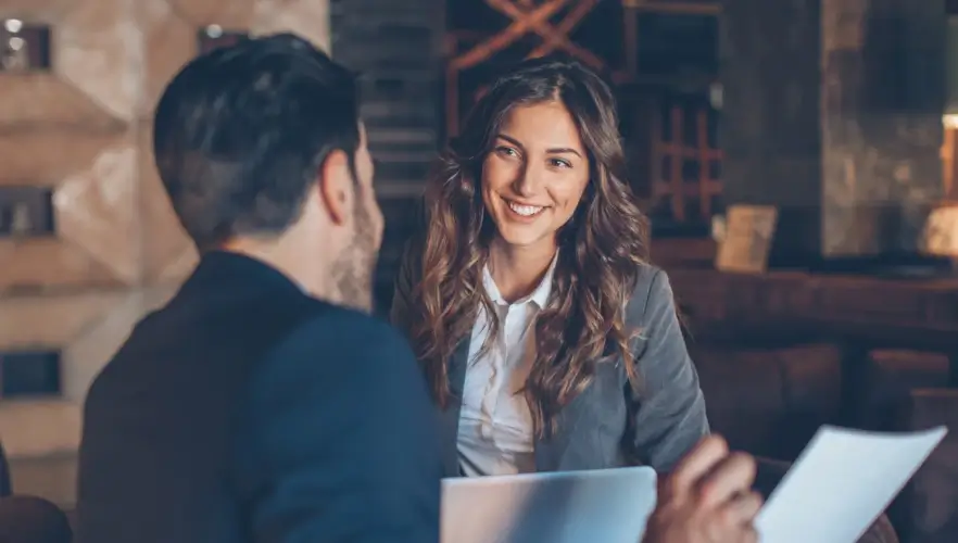 Two professionals engaged in a friendly conversation, with the woman smiling warmly while holding documents.