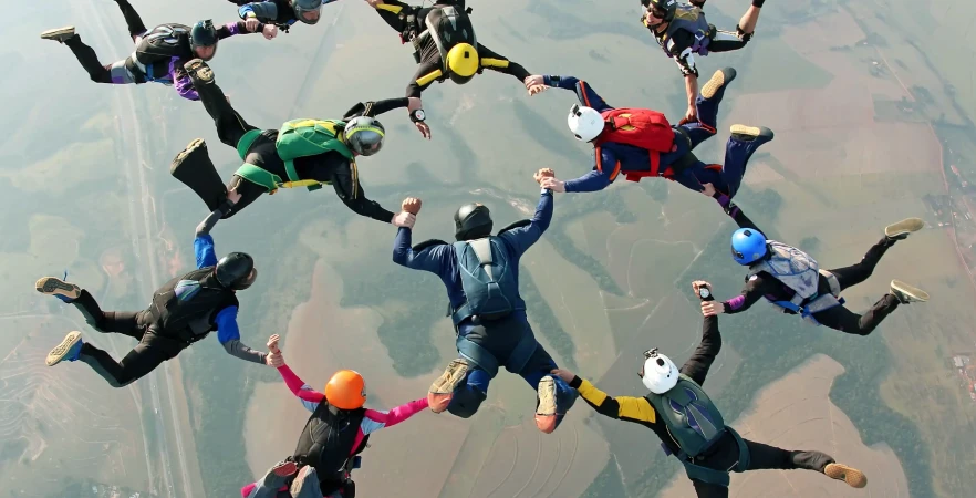 Skydivers in colorful gear form a circle while free-falling against a backdrop of a hazy earth below.