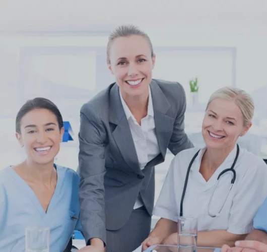 A diverse group of three smiling professionals: a businesswoman in a suit and two healthcare workers in scrubs and a white coat with a stethoscope. Bright, positive atmosphere.