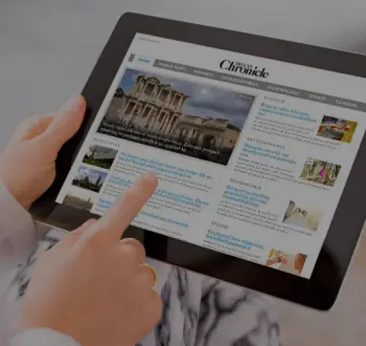 A person holding a tablet and browsing an online news website. Their finger is pointing at the screen, which displays various news articles and images.