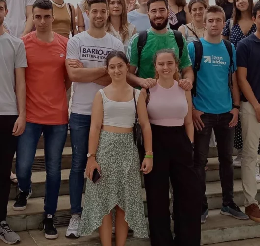 A group of young adults poses on stairs, smiling and relaxed. They wear casual clothes in various colors, conveying a friendly and social atmosphere.