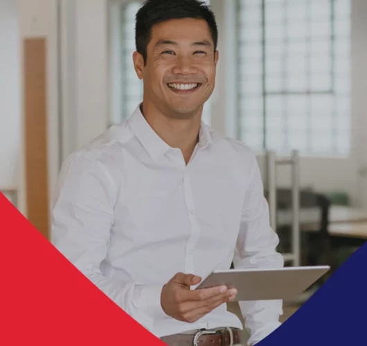 Smiling man in a white shirt holding a tablet in a modern office. Red and blue geometric design on the bottom edges adds a professional tone.