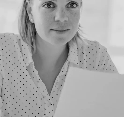 Black and white image of a woman with a focused expression, holding a document. She is wearing a polka-dot blouse, conveying a professional tone.