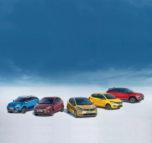 Five colorful cars are parked on a vast, white surface under a clear blue sky. The vibrant car colors create a dynamic, inviting scene.