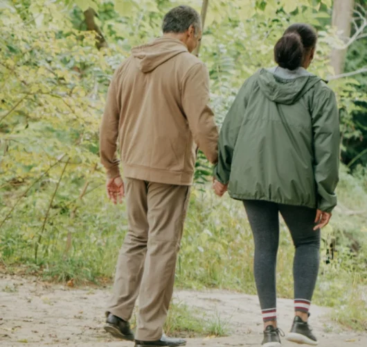 An old man and a young caregiver woman walking hand in hand, surrounded by the tranquillity of nature