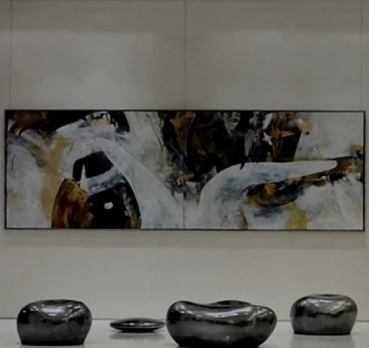 A modern lobby with abstract art on the wall, featuring swirling gray, white, and brown tones. Below the painting are four glossy, black, pebble-shaped seats arranged on a white floor.